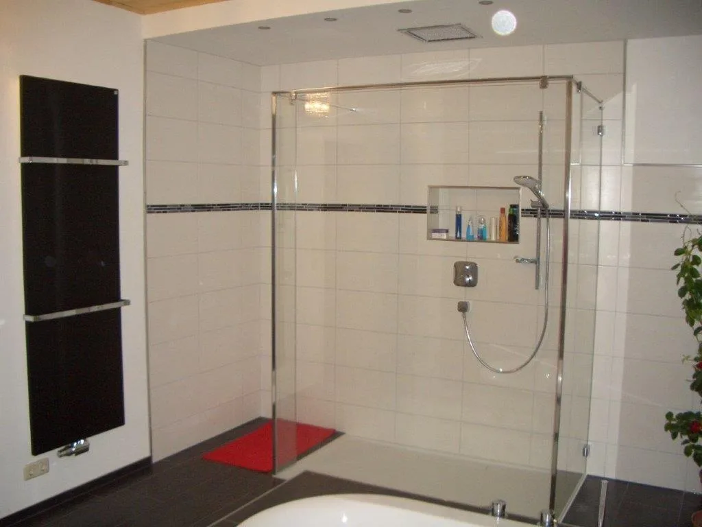 Fertiges Badezimmer mit bodengleicher Dusche hinter einer Glaswand und schwarzem Heizkörper
