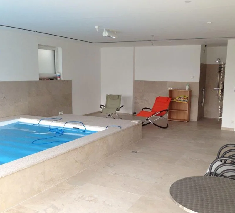 Innenschwimmbecken in einem gefliesten Raum mit Liegen und einer Dusche an der Wand