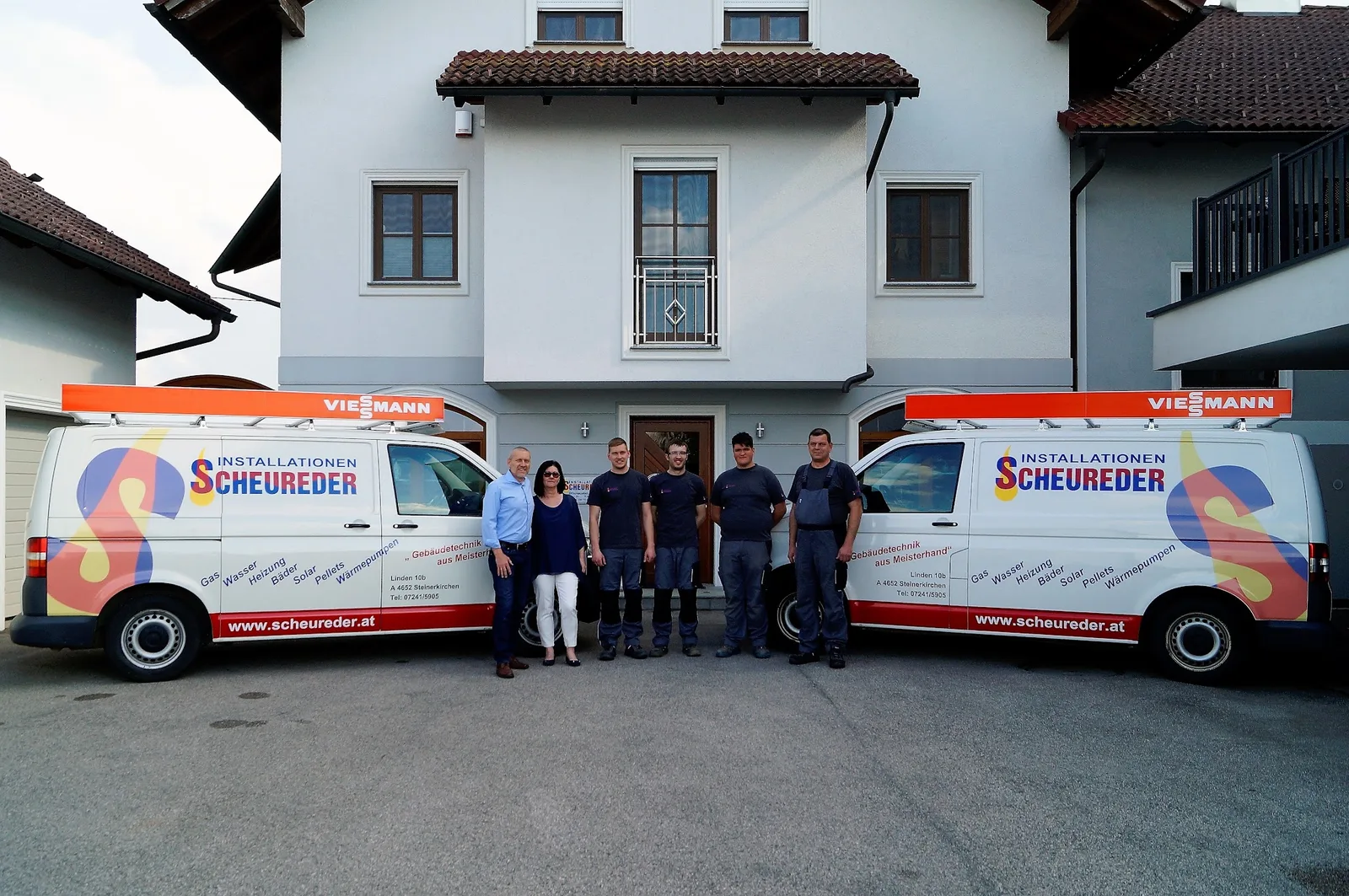 Das Team vor dem Firmengebäude zwischen zwei beschrifteten Transportern mit Dachträgern