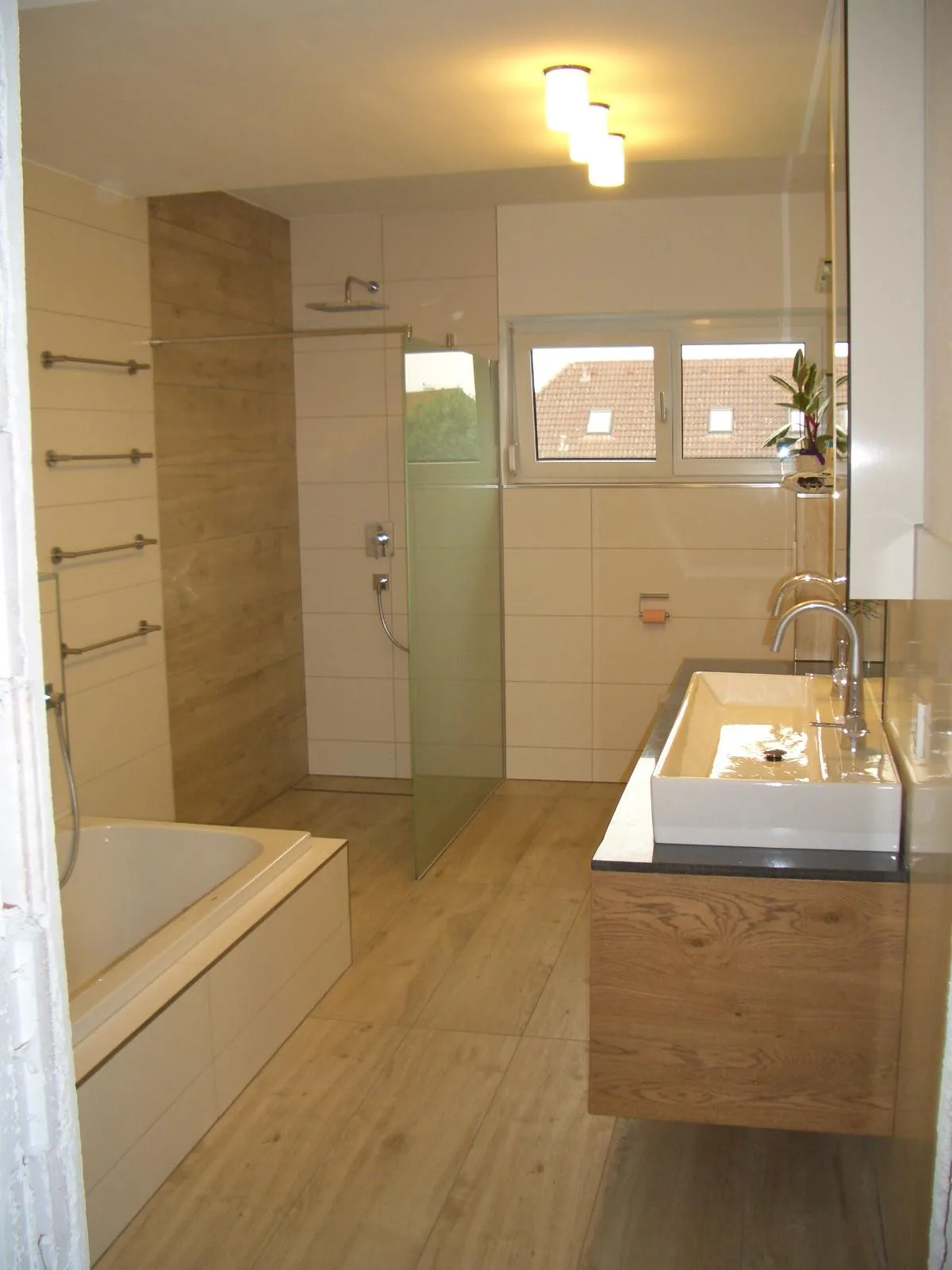 Fertiges Badezimmer mit Wanne, bodengleicher Dusche und Waschtisch auf einem Holzunterbau