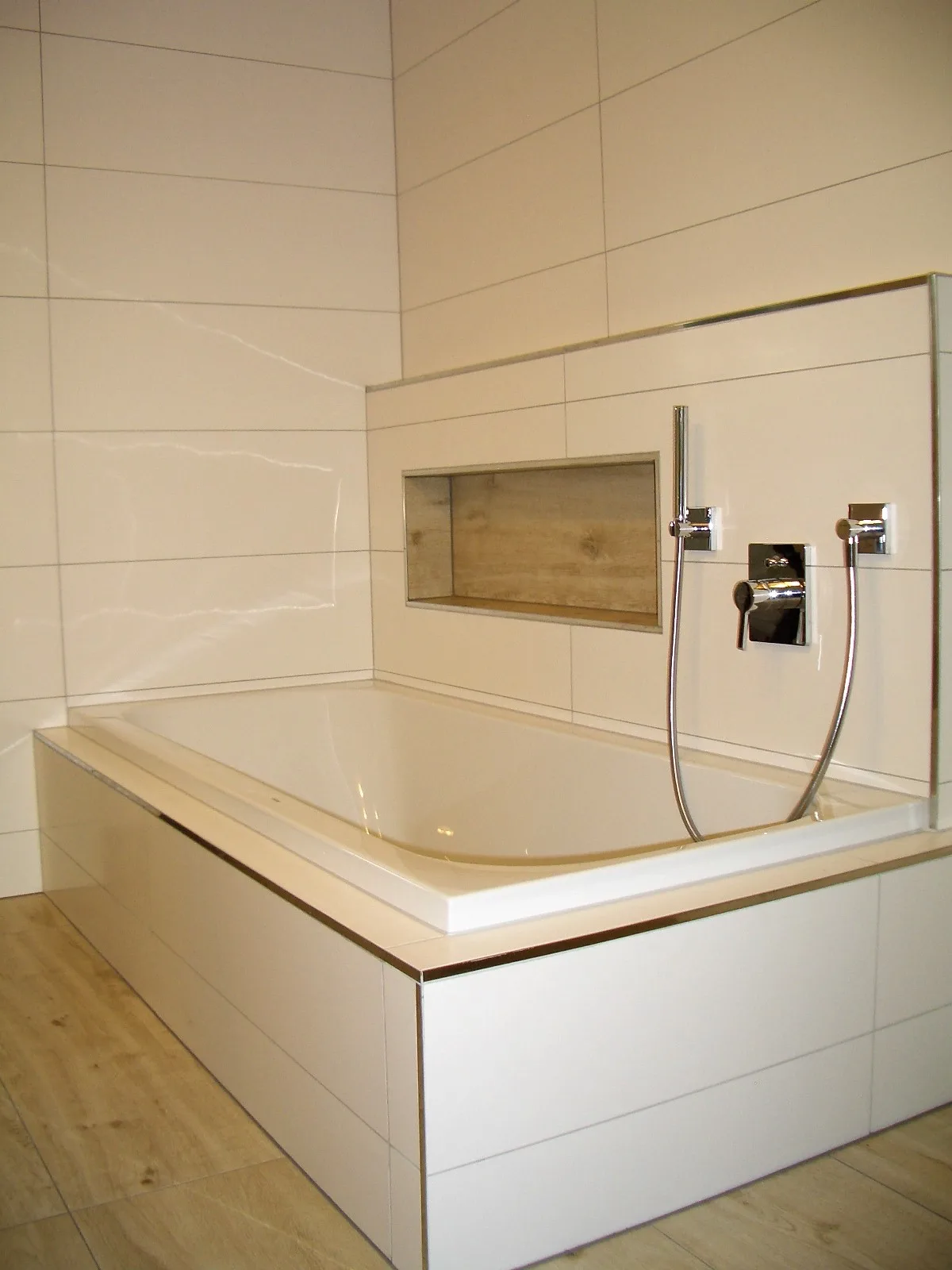 Badewanne mit gefliester Ablagenische und Armaturen in hellen Fliesen
